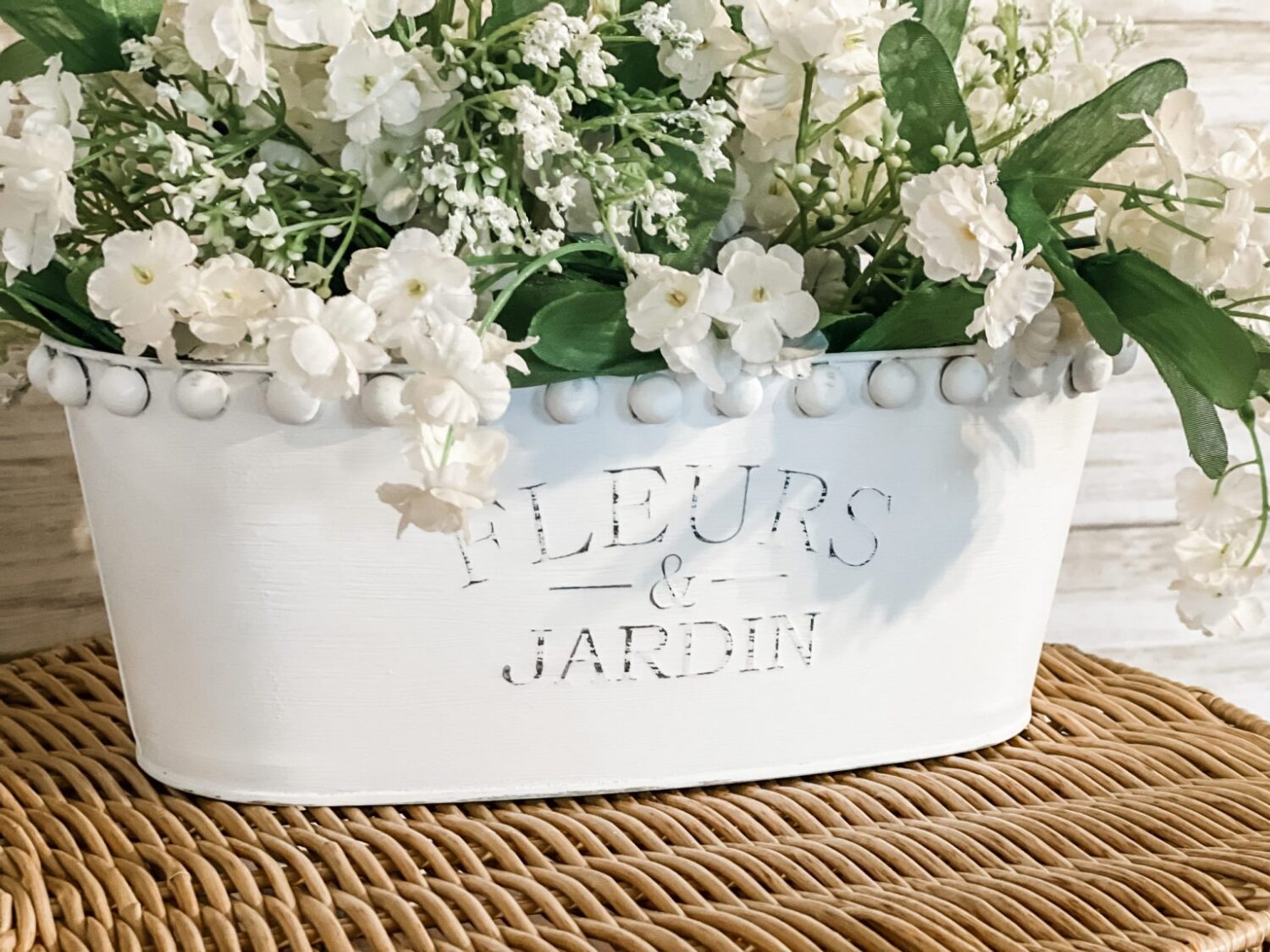 DIY Dollar Tree farmhouse planter.  A silver bin with white chalk paint and beads glued around the top edge, filled with flowers.