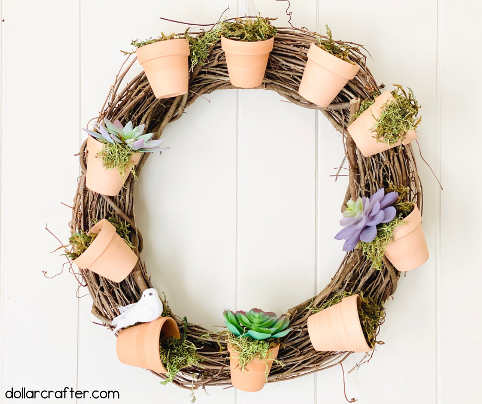 DIY wreath using Dollar Tree mini terracotta pots.  The pots are arranged all around the wreath and holding small succulents and moss.